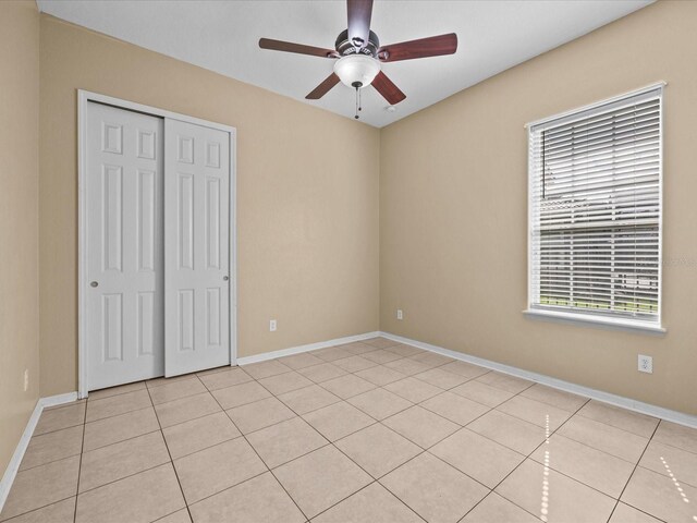 unfurnished bedroom with light tile patterned floors, ceiling fan, a closet, and baseboards