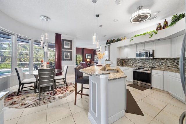 kitchen with light stone counters, sink, decorative light fixtures, a kitchen island with sink, and appliances with stainless steel finishes