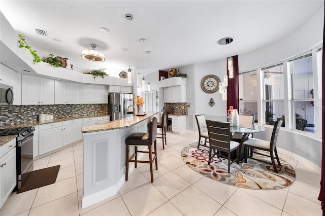 kitchen featuring white cabinetry, an island with sink, stone countertops, stainless steel appliances, and decorative light fixtures