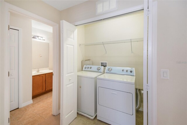 clothes washing area with washing machine and dryer, light tile patterned flooring, and sink