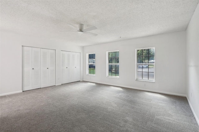 unfurnished bedroom featuring multiple windows, a textured ceiling, two closets, and ceiling fan