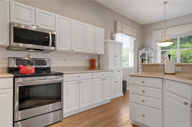 kitchen with appliances with stainless steel finishes, decorative backsplash, light countertops, light wood-type flooring, and pendant lighting