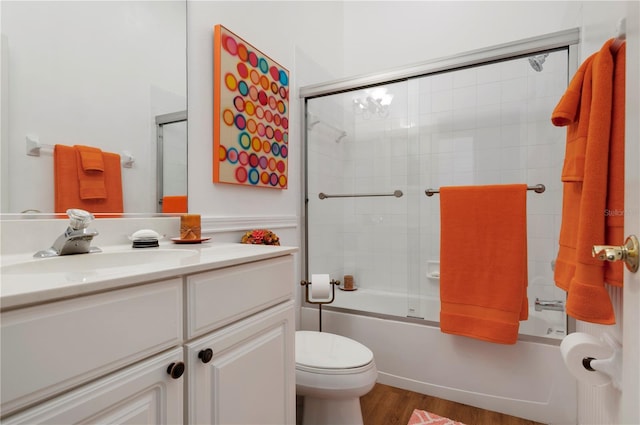 bathroom with wood finished floors, vanity, toilet, and bath / shower combo with glass door