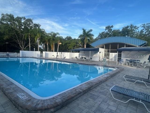 community pool with a patio, fence, and view of wooded area