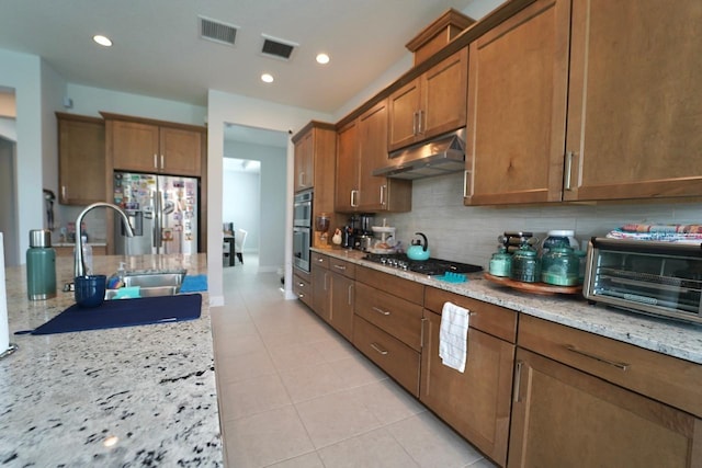 kitchen with backsplash, light tile patterned floors, sink, light stone countertops, and appliances with stainless steel finishes