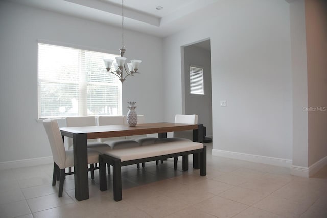 dining area with a healthy amount of sunlight, a notable chandelier, a tray ceiling, and light tile patterned flooring