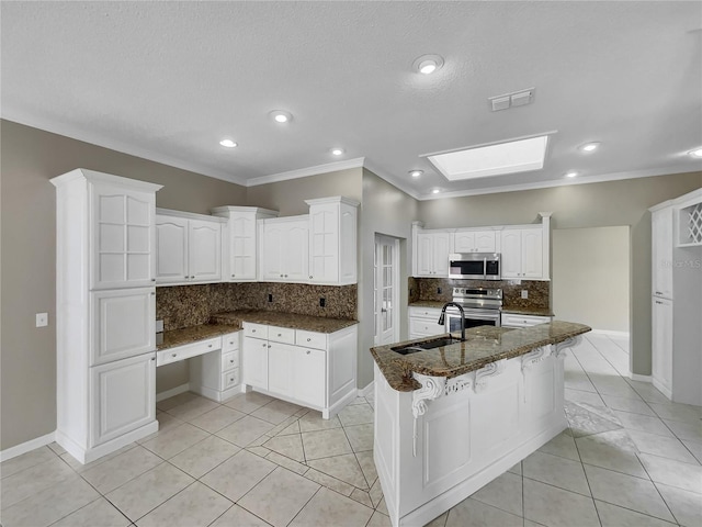 kitchen featuring dark stone countertops, white cabinetry, stainless steel appliances, decorative backsplash, and a center island with sink