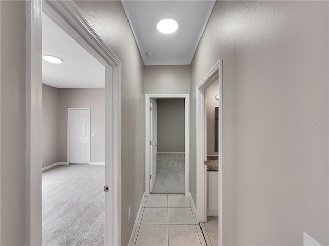 hallway featuring light tile patterned floors, baseboards, and light carpet