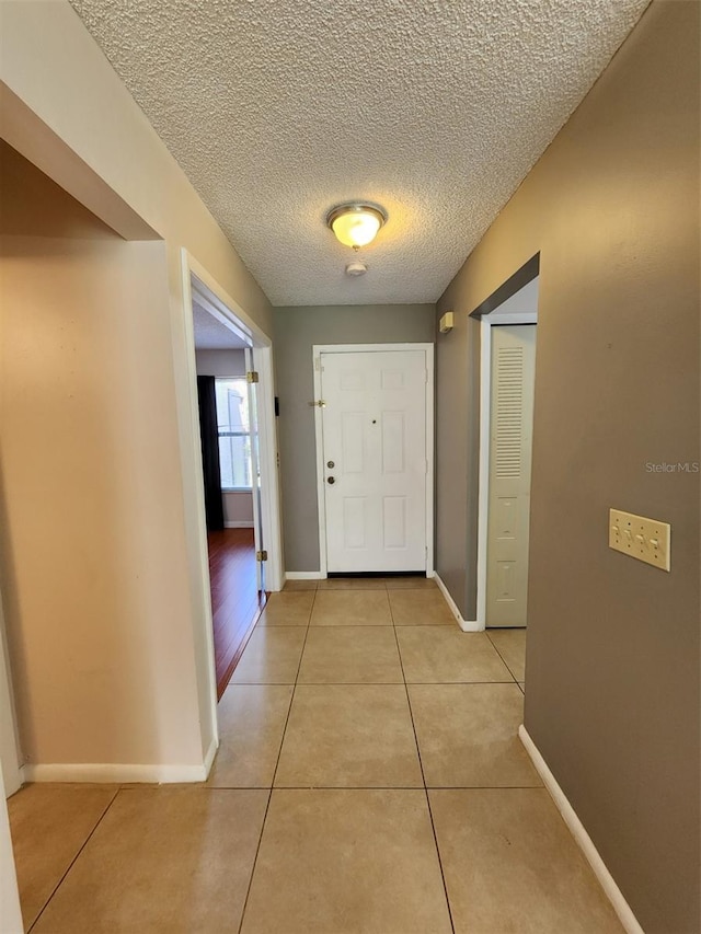 doorway with a textured ceiling and light tile patterned flooring