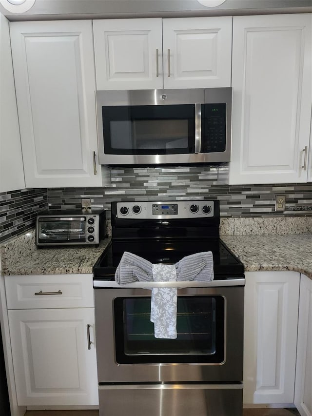 kitchen featuring stainless steel appliances, light stone counters, decorative backsplash, and white cabinets