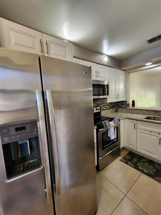 kitchen with light tile patterned floors, light stone countertops, stainless steel appliances, white cabinetry, and sink