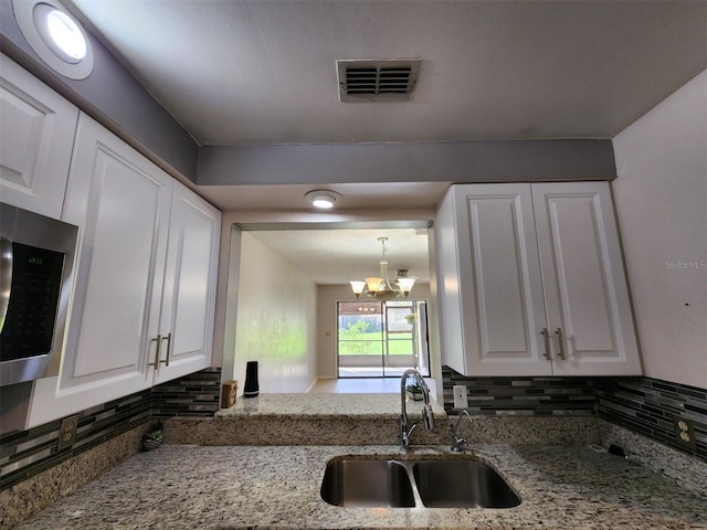 kitchen with light stone counters, sink, white cabinets, and a notable chandelier