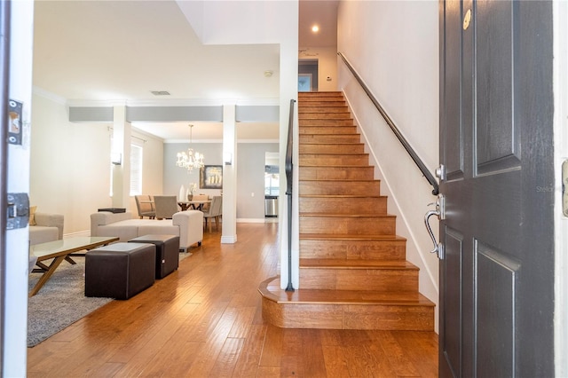 staircase featuring wood-type flooring, ornamental molding, a chandelier, and plenty of natural light