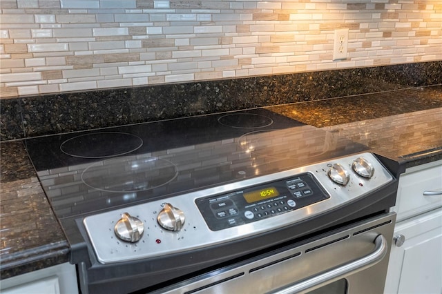 interior details featuring decorative backsplash, electric range, white cabinets, and dark stone countertops