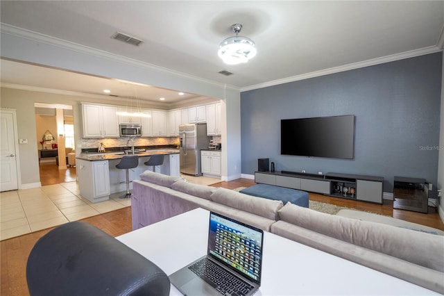 tiled living room featuring ceiling fan, crown molding, and sink