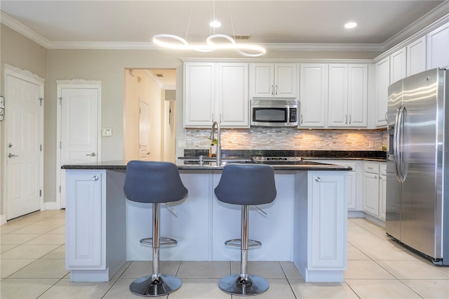 kitchen with stainless steel appliances, crown molding, a center island with sink, and white cabinetry