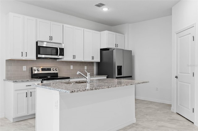 kitchen featuring stainless steel appliances, light stone countertops, white cabinetry, and a kitchen island with sink