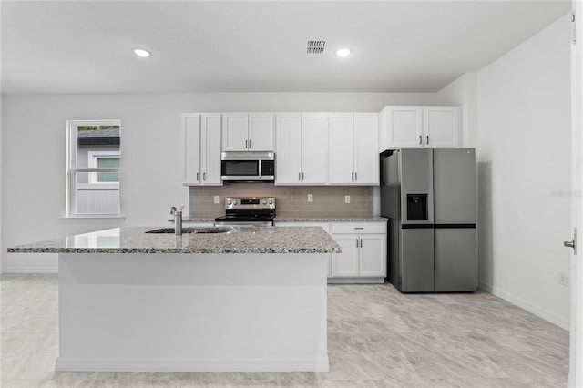 kitchen with stainless steel appliances, light stone counters, and a kitchen island with sink