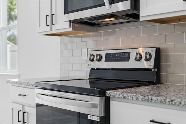 kitchen with light stone countertops, appliances with stainless steel finishes, white cabinetry, and decorative backsplash