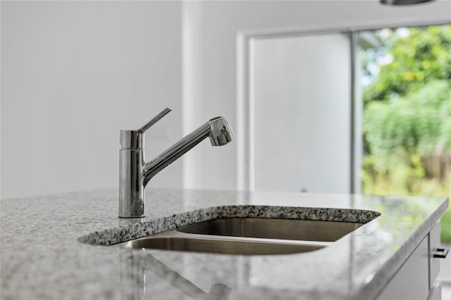 room details with white cabinets, light stone counters, and sink