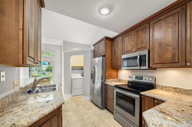 kitchen with sink, light stone countertops, appliances with stainless steel finishes, lofted ceiling, and washer / clothes dryer