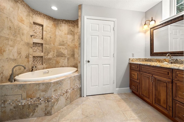 bathroom featuring a textured ceiling, tiled bath, and vanity