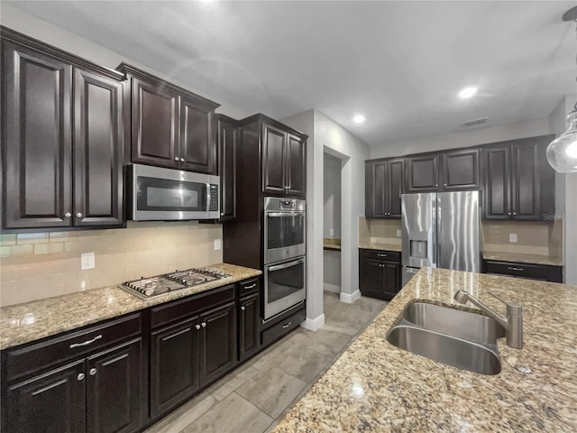 kitchen with light stone counters, stainless steel appliances, sink, tasteful backsplash, and dark brown cabinetry