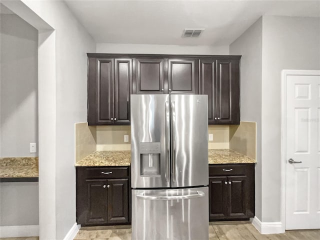 kitchen with light stone countertops, light wood-type flooring, stainless steel fridge with ice dispenser, and dark brown cabinetry