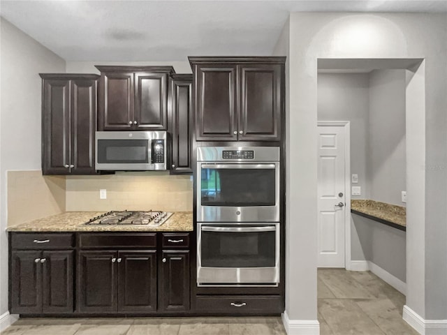 kitchen with stainless steel appliances, light stone counters, dark brown cabinets, and tasteful backsplash