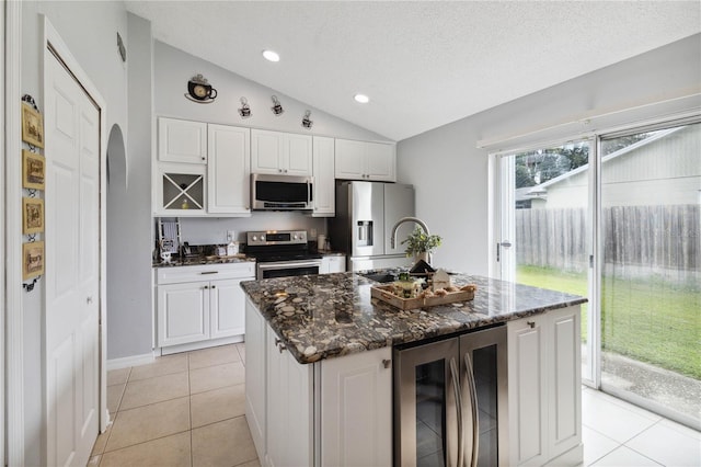 kitchen with vaulted ceiling, an island with sink, white cabinets, beverage cooler, and stainless steel appliances