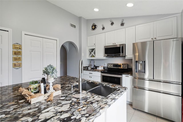 kitchen with appliances with stainless steel finishes, sink, dark stone countertops, white cabinets, and light tile patterned floors