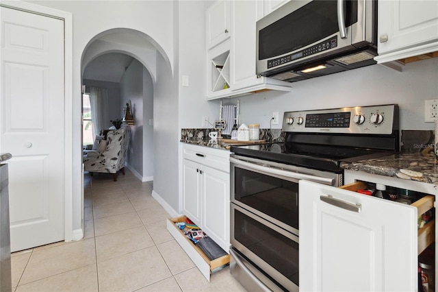 kitchen featuring white cabinets, appliances with stainless steel finishes, dark stone counters, and light tile patterned floors