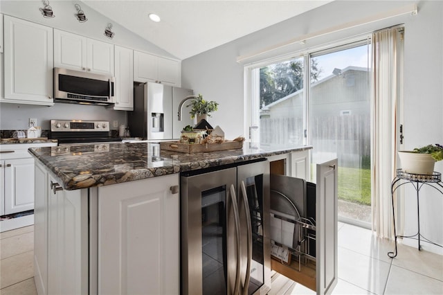 kitchen with light tile patterned floors, appliances with stainless steel finishes, a center island, white cabinets, and vaulted ceiling