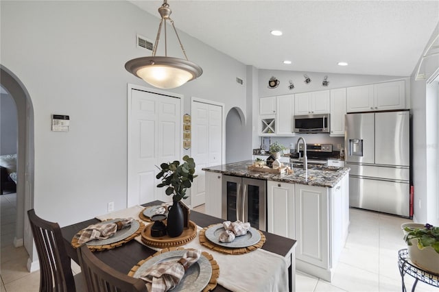 kitchen with appliances with stainless steel finishes, white cabinetry, dark stone countertops, an island with sink, and decorative light fixtures