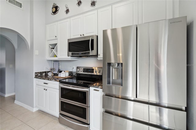 kitchen featuring stainless steel appliances, white cabinetry, dark stone countertops, and light tile patterned flooring