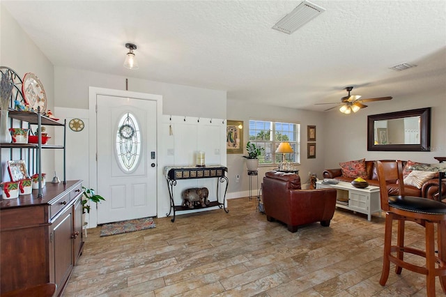 foyer featuring a ceiling fan, a textured ceiling, visible vents, and light wood finished floors