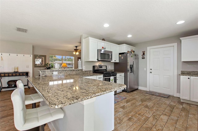 kitchen with appliances with stainless steel finishes, a breakfast bar area, a peninsula, a ceiling fan, and visible vents
