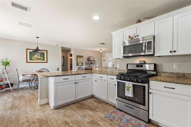 kitchen featuring white cabinets, appliances with stainless steel finishes, a textured ceiling, dark stone counters, and a peninsula