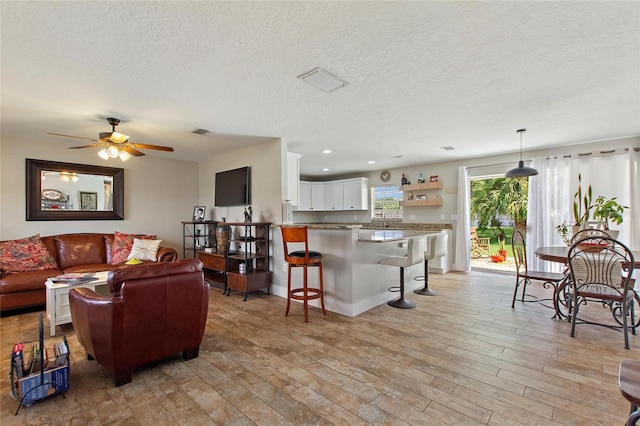 living room with recessed lighting, a textured ceiling, ceiling fan, and light wood-style flooring