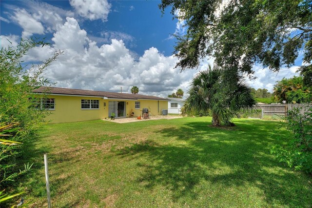 rear view of property featuring a yard, fence, and stucco siding