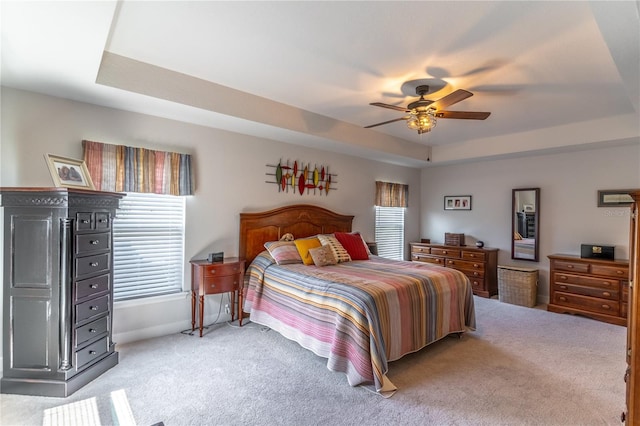 bedroom with ceiling fan, a raised ceiling, and multiple windows