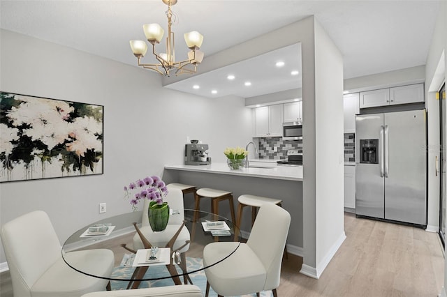 dining area featuring a notable chandelier, sink, and light hardwood / wood-style floors