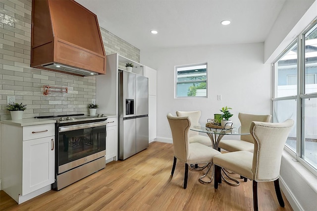 kitchen with white cabinetry, vaulted ceiling, appliances with stainless steel finishes, custom range hood, and light hardwood / wood-style floors