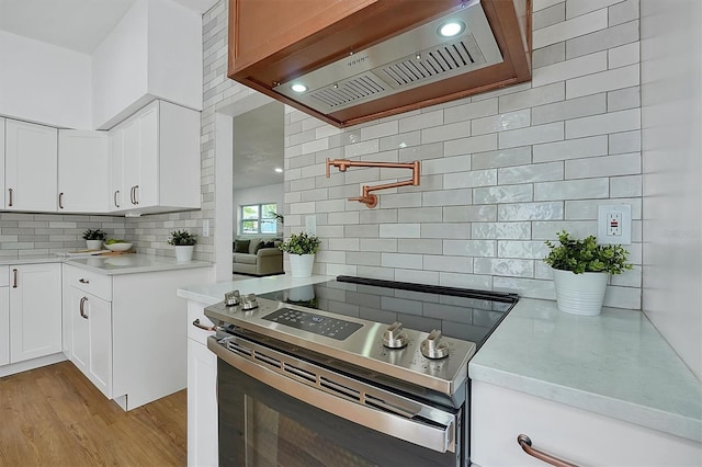 kitchen with stainless steel electric range, light hardwood / wood-style floors, custom range hood, and white cabinets