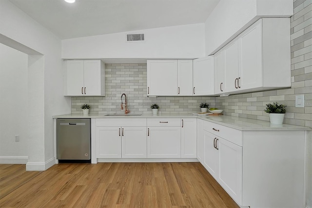 kitchen with white cabinets, vaulted ceiling, stainless steel dishwasher, and sink