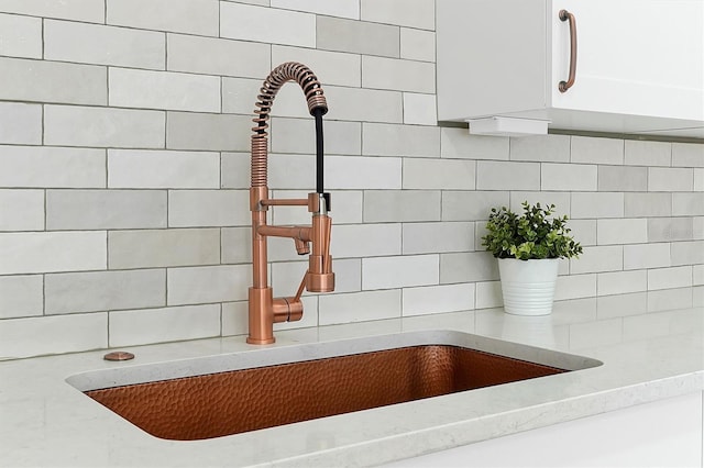 room details with white cabinets, light stone countertops, and sink