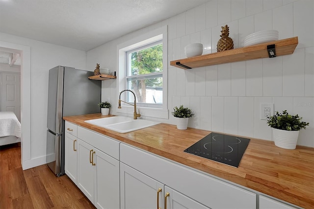 kitchen with white cabinetry, wooden counters, sink, black electric cooktop, and light hardwood / wood-style floors