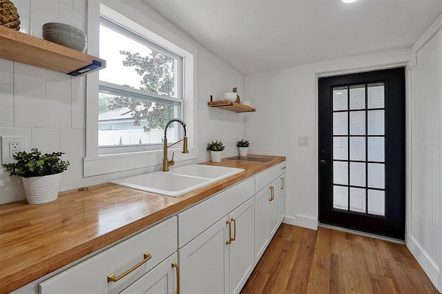 kitchen with sink, wood counters, white cabinetry, and light hardwood / wood-style floors