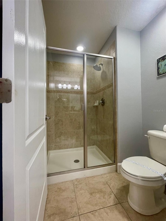 bathroom featuring toilet, an enclosed shower, tile patterned floors, and a textured ceiling