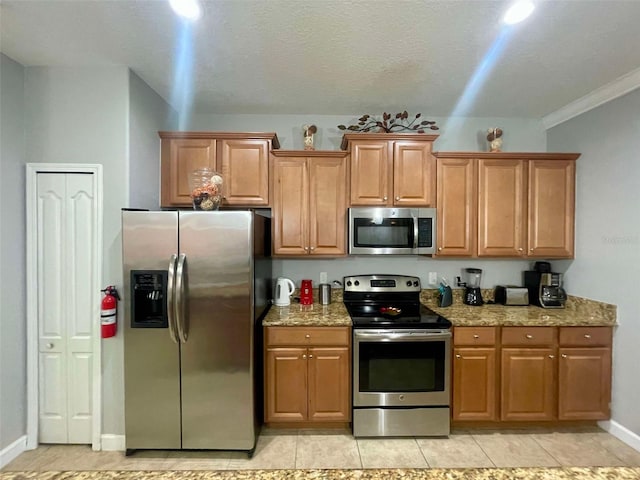 kitchen featuring crown molding, a textured ceiling, light tile patterned floors, light stone counters, and appliances with stainless steel finishes